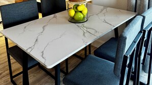 Et spiseområde med et marmorbord, stole, en dekorativ glasbeholder med citroner, en sofa og en potteplante.