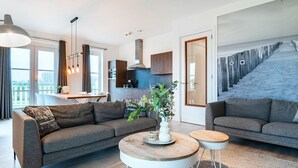Una sala de estar moderna con un sofá gris, una mesita de centro y un comedor con cocina al fondo.