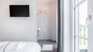 Una habitación de hotel moderna con cama, televisor, ducha y vistas al exterior.
