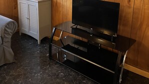 A room with wooden walls, a window with a view of trees, a white cabinet, and a black entertainment unit with a television.