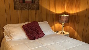 A neatly made bed with a white duvet and a red throw pillow in a room with wooden paneling.