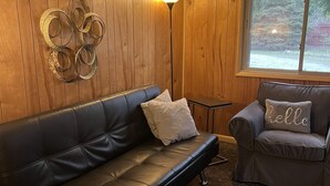 A room with a black leather sofa, a grey armchair, a small table, and a floor lamp.