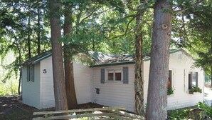 A small, single-story house with a gabled roof, surrounded by trees.