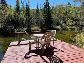 A wooden deck with a table and chairs overlooking a river. - Sleeping Bear Riverside Cabins - Cabin #5 (Honor)
