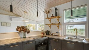 A modern kitchen with dark cabinetry, a built-in oven, and a large window offering a view of the outdoors. - 2 bedroom cozy home in Askø (Askø)
