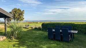 A grassy outdoor area with a table and chairs, a wooden fence, and a view of the sea. - 2 bedroom cozy home in Askø (Askø)