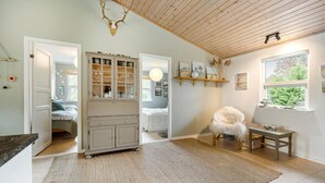 A cozy room with a wooden ceiling, a large cabinet with glass doors, a fluffy chair, and a window with a view of greenery. - 2 bedroom cozy home in Askø (Askø)