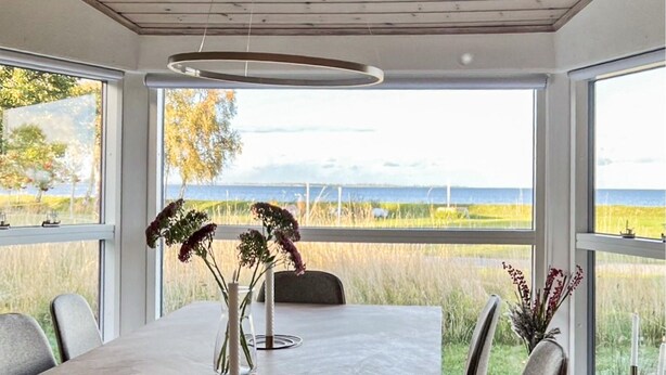 A dining area with a table, chairs, and a view of the sea through large windows. - 2 bedroom cozy home in Askø (Askø)