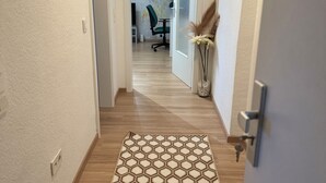 A hallway with a patterned rug, a door with a keyhole, and a room with a plant and a chair in the background. - Be Home in Dortmund (Dortmund)