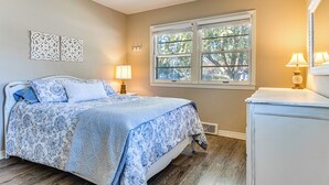 Un dormitorio con cama, lámparas de noche, cómoda y ventana con vista a árboles.