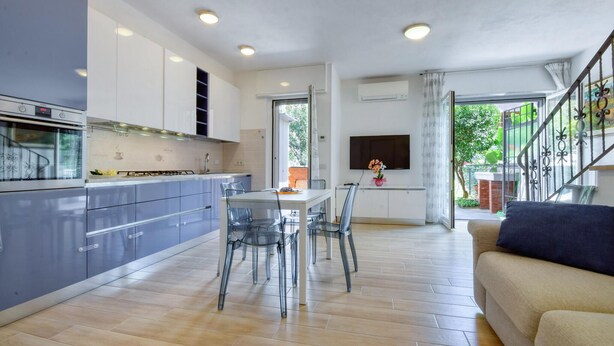 A modern kitchen with a dining area, a sofa, and a staircase leading to an outdoor area.