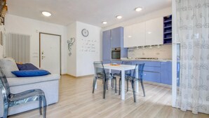 A modern kitchen with a dining area, featuring a white table, clear chairs, and a blue cabinet.