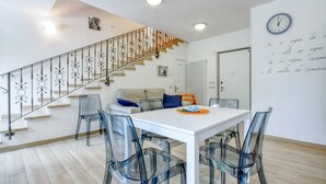 A modern living space with a staircase, a dining area with clear chairs, a sofa, and a wall clock.