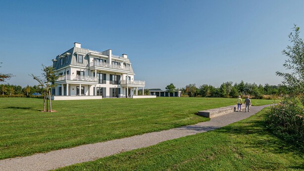 A large, multi-story building with a symmetrical facade, a central entrance, and a surrounding lawn.