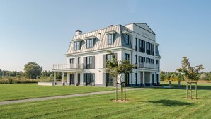 A large, two-story house with a white exterior and dark shutters, featuring a balcony and a well-maintained lawn.
