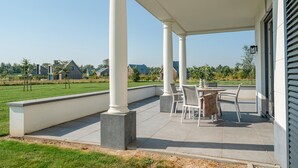 A covered patio with a table and chairs, columns, and a view of houses in the background.