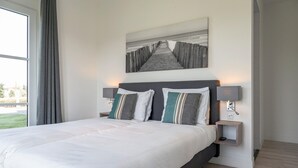 A modern hotel room with a large bed, two bedside tables, a wall-mounted artwork, and a view of the outdoors.