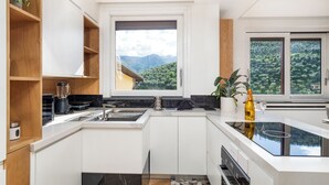 A modern kitchen with white cabinets, a black countertop, and a window overlooking a mountainous landscape.
