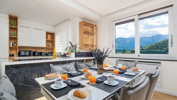 A modern kitchen with a dining area, a large window with a mountain view, and breakfast items on the table.