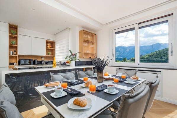 Une cuisine moderne avec un coin repas, une grande fenêtre donnant sur les montagnes et des aliments pour le petit-déjeuner disposés sur la table.