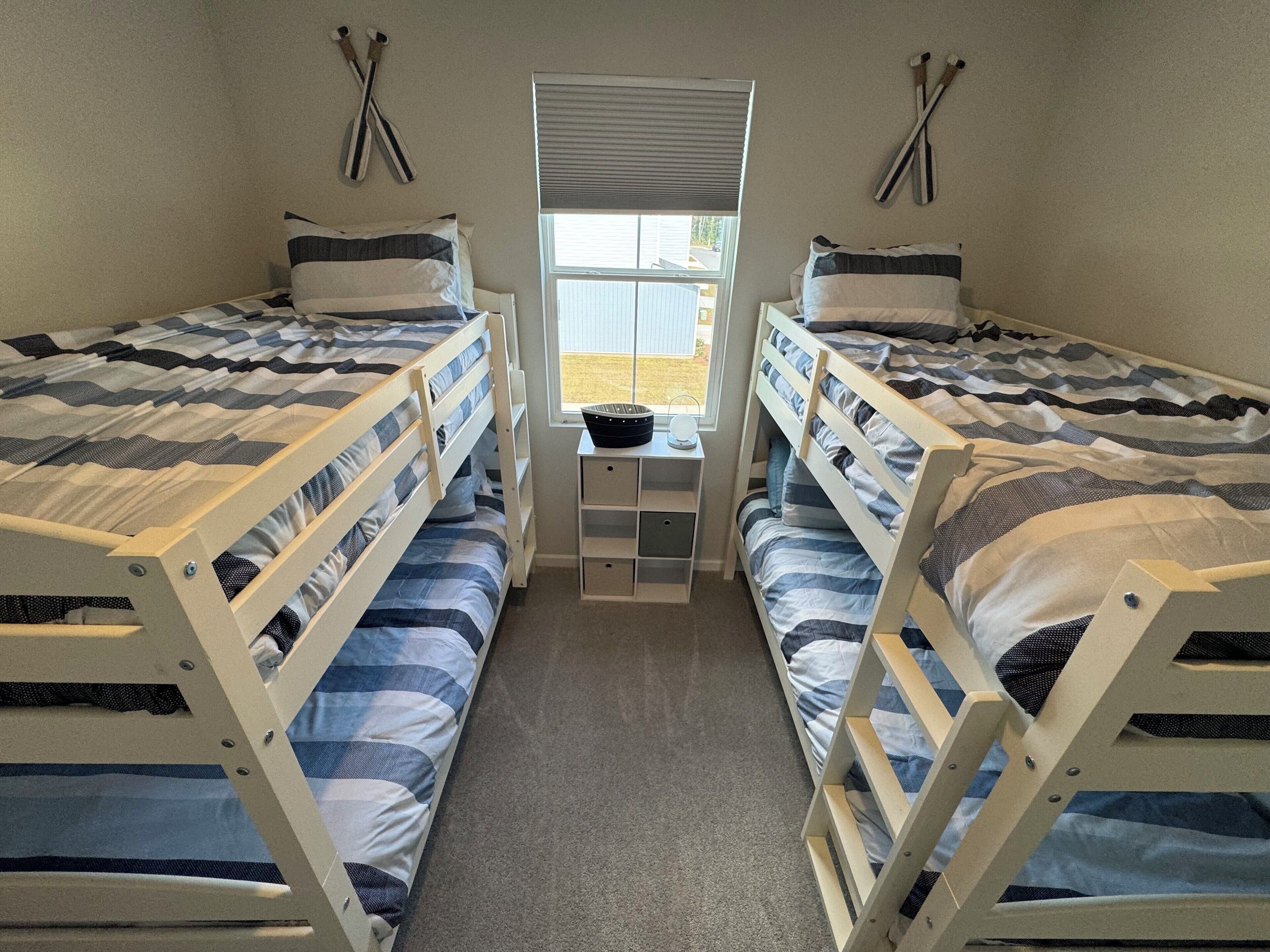 Une chambre avec deux lits superposés, une petite table et une fenêtre avec des stores.