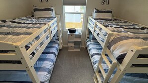 Une chambre avec deux lits superposés, une petite table et une fenêtre avec des stores.