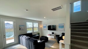 Un salon moderne avec un canapé d’angle, un téléviseur à écran plat et un escalier.