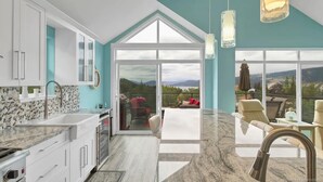 A modern kitchen with a large window, a dining area with a view, and a balcony with outdoor seating. - La Casa Cottage Beach Vibe, Entire Home Lake Views (Kelowna)