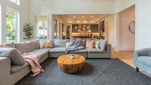 A spacious living room with a large sectional sofa, a round wooden coffee table, and a grey carpet. - Bellevue Dream w/ Spacious 6BR Luxury Home (Bellevue)