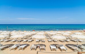 Ein Strand mit Liegestühlen und Sonnenschirmen, einem klaren blauen Himmel und dem Meer im Hintergrund.