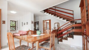 Ein Essbereich mit Holztisch und -stühlen, eine Treppe mit hölzernen Geländern und ein Ausblick ins Freie durch ein Fenster.