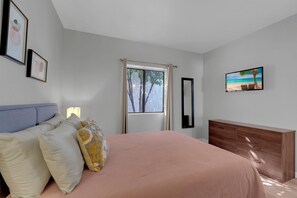 A bedroom with a bed, a dresser, a window with curtains, and a wall-mounted TV. - City Center Townhouse with Private Yard! (Tucson)