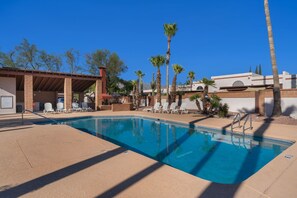 A swimming pool with lounge chairs, palm trees, and a covered patio area.