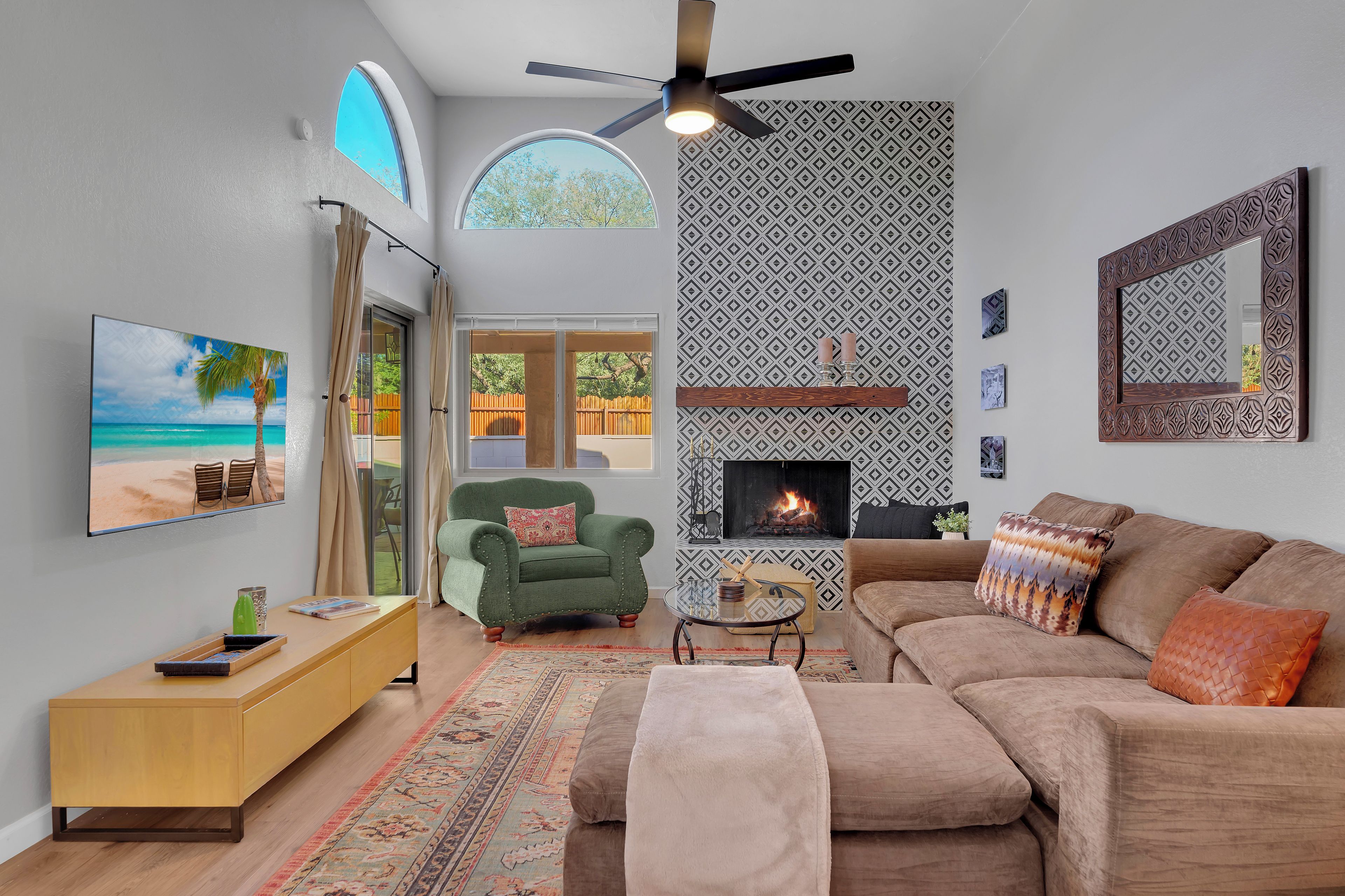 A living room with a fireplace, a sofa, a green armchair, a TV, and a view of the outdoors through a window.