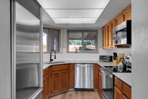 A modern kitchen with stainless steel appliances, wooden cabinets, and a window providing natural light.