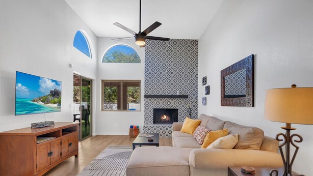 A modern living room with a fireplace, a large TV, and a ceiling fan. - City Center Townhouse with Private Yard! (Tucson)