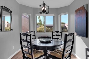 A dining area with a round table, six chairs, a chandelier, and a view of the outside through large windows. - City Center Townhouse with Private Yard! (Tucson)