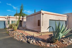 A stucco building with a garage, a stone pathway, and desert landscaping.