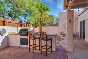 An outdoor patio with a grill, two wooden chairs, a palm tree, and a view of the backyard. - City Center Townhouse with Private Yard! (Tucson)