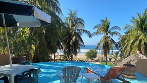 A poolside area with lounge chairs and a table, overlooking a beach with palm trees and the ocean. - Casa Pelicanos is a private beachfront home with pool. Short walk to town.
 (Troncones)