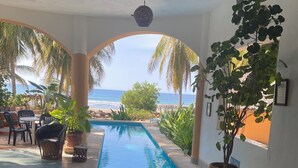 A pool area with a view of the ocean, surrounded by palm trees and potted plants. - Casa Pelicanos is a private beachfront home with pool. Short walk to town.
 (Troncones)