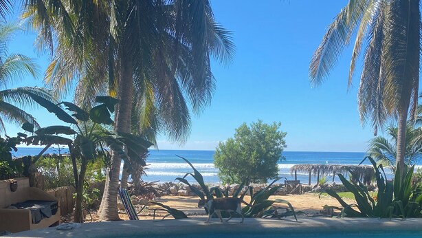 A beach view with palm trees, a sandy area, and a small structure. - Casa Pelicanos is a private beachfront home with pool. Short walk to town.
 (Troncones)