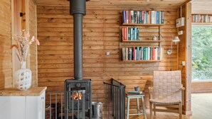 Een gezellig houten huisje interieur met een houtkachel, boekenkasten, een rieten mand en een stoel.
