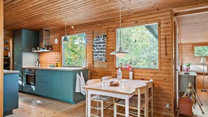 Een modern houten interieur met een houten plafond, een keuken met turquoise kastjes, een eethoek met een houten tafel en stoelen, en grote ramen met uitzicht op de natuur.