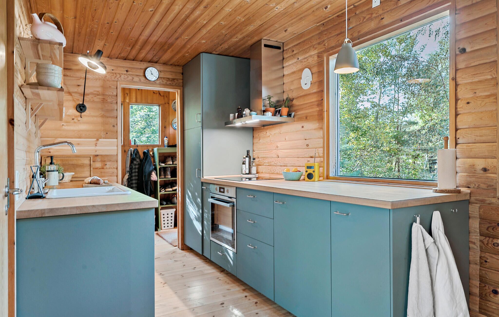 A modern kitchen with wooden walls, a large window, and a view of greenery.