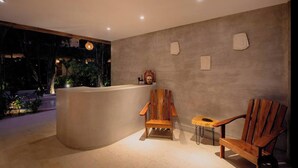 A reception area with a curved reception desk, two wooden chairs, a small table, and a wall-mounted sculpture. - HEAVENLY MAYAN ESCAPE CHIC 1 BDRM APT 250 MB WiFi IN HEART OF TULUM, PLUNGE POOL (Tulum)