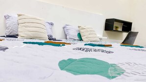 Ein Bett mit einer gemusterten Decke, Kissen und einem Nachttisch mit einer Pflanze.