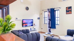 Ein modernes Wohnzimmer mit Flachbildfernseher, grauen Sofas, einem Holztisch und einer Topfpflanze.