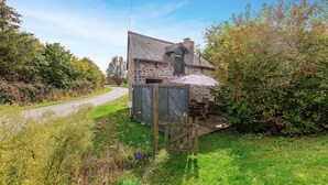 A stone house with a sloped roof, a wooden fence, and a garden area with various plants and a wooden deck. - Lovely home in Mont-Dol with WiFi (Mont-Dol)