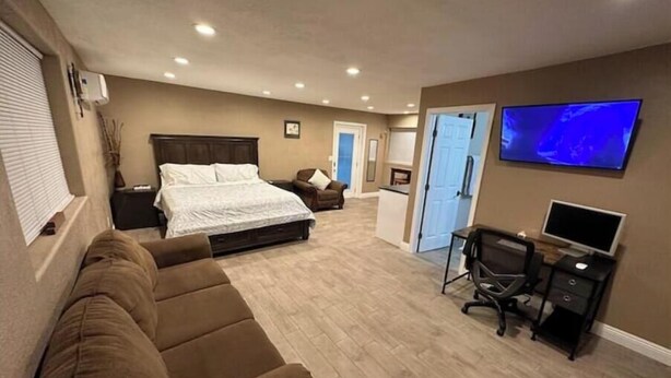 Ein Schlafzimmer mit einem Bett, einem braunen Sofa, einem Schreibtisch mit Computer und einem Fernseher an der Wand.